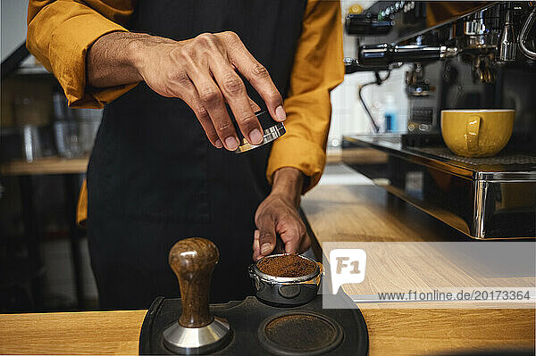 Barista tamping ground coffee in portafilter with tamper at cafe