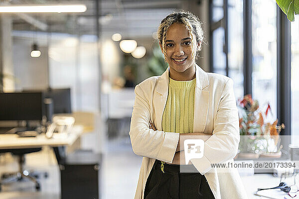 Smiling young businesswoman standing with arms crossed at office