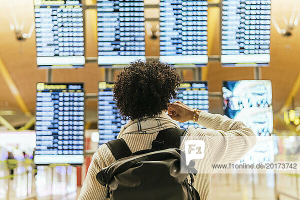 Man with curly hair looking at arrival departure board at airport