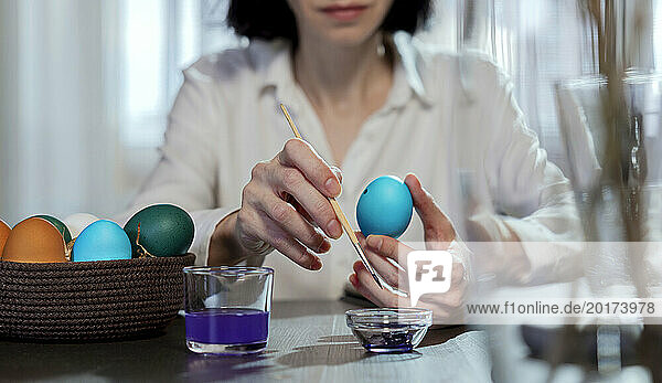 Woman painting color on easter egg at home