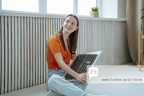 Smiling young woman sitting with solar panel at home