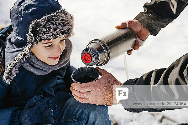 Father pouring hot tea in cup for son in winter