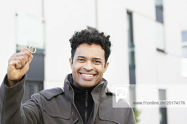 Happy man holding key of new house in front of building