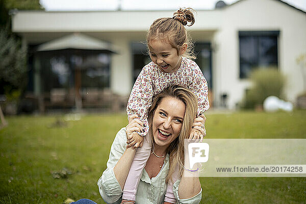 Happy mother with daughter sitting on shoulders near house