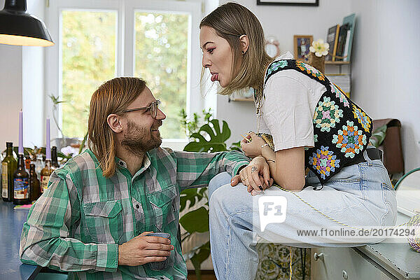 Woman teasing happy man sitting at home