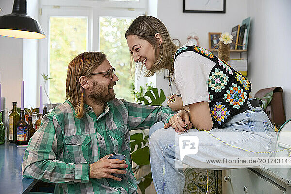 Happy man holding coffee cup and sitting with woman at home