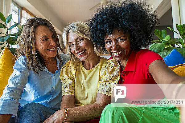 Happy mature woman taking selfie with multiracial friends sitting on sofa at home