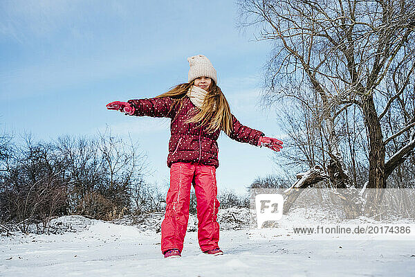 Happy girl standing with arms outstretched on snow in winter