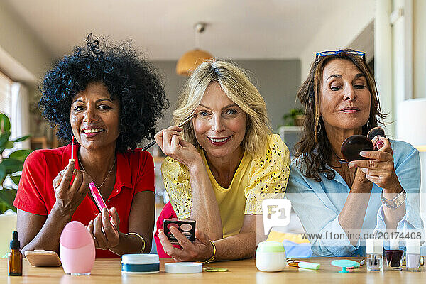 Beautiful multiracial friends applying make-up at home