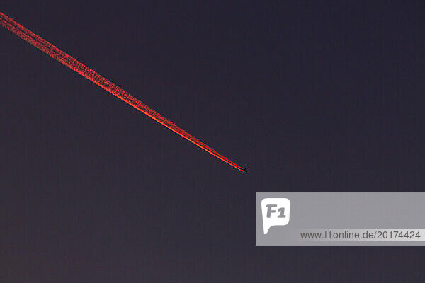 Airplane leaving red vapor trail against sky at night