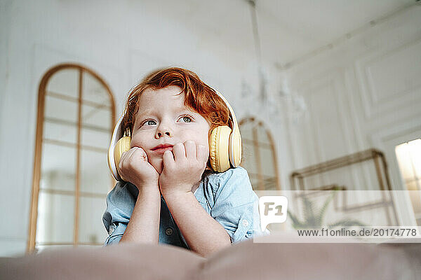 Redhead boy leaning on elbows and listening to music at home