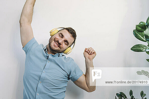 Cheerful man listening to music through wireless headphones and dancing at home