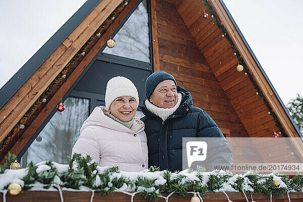 Smiling woman with man outside log cabin in winter
