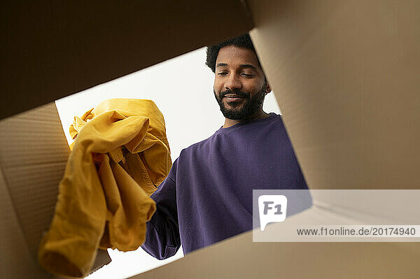 Smiling young man putting clothes in cardboard box