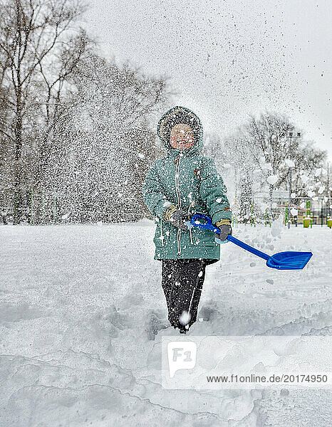 Cheerful boy holding shovel toy and playing with snow at park