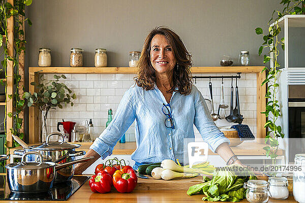 Smiling senior woman standing by vegetable on kitchen counter at home