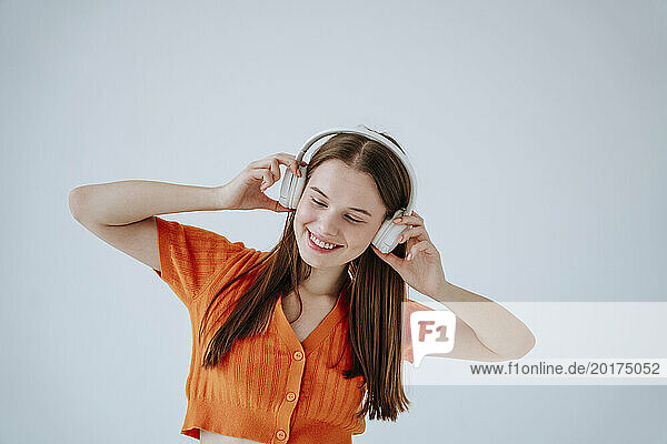 Smiling woman with eyes closed listening to music against white background