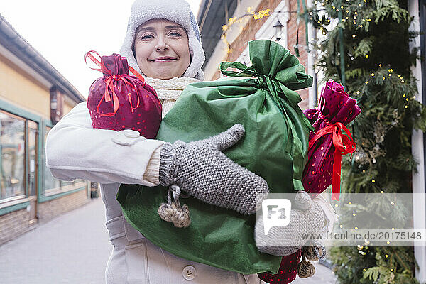Smiling woman carrying gift bags at street in Christmas