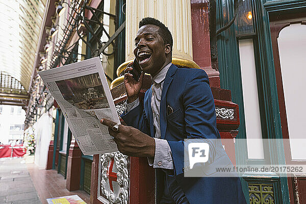 Happy businessman reading newspaper and talking on smart phone