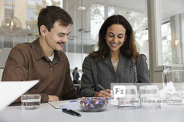 Man looking at smiling woman signing agreement at desk in real estate office