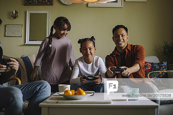 Portrait of happy gay couple playing video game with daughter while sitting on sofa at home