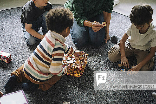 High angle view of schoolboys playing puzzle game with female teacher in classroom at kindergarten