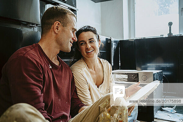 Happy couple discussing over wood in kitchen while renovating home