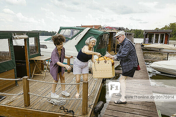 Full length of man giving basket to woman on houseboat against sky