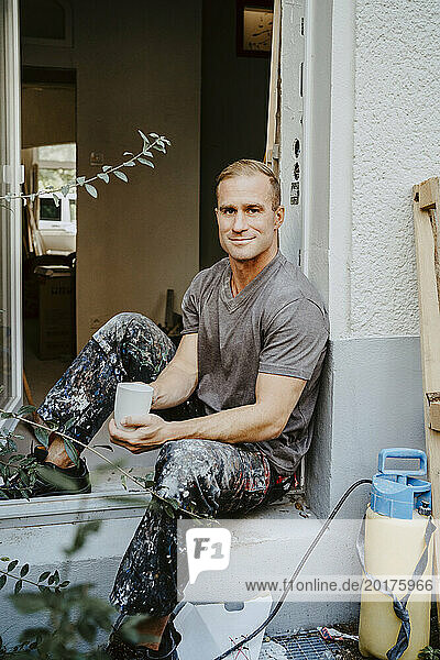 Portrait of smiling male carpenter holding coffee cup at doorway of house