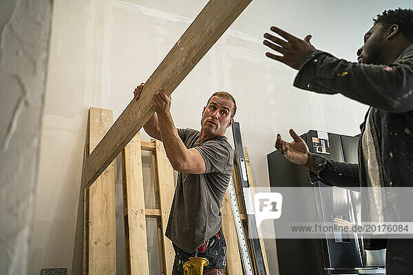 Multiracial male carpenters carrying plank while working in apartment