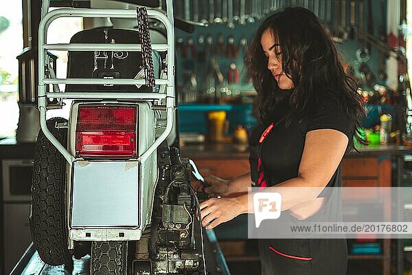 Eine hispanische junge sinnliche Mechanikerin  die ein Rücklicht in einer Autowerkstatt inspiziert  eine Latino Frau in einem traditionellen männlichen Berufskonzept  weibliche Macht im wirklichen Leben