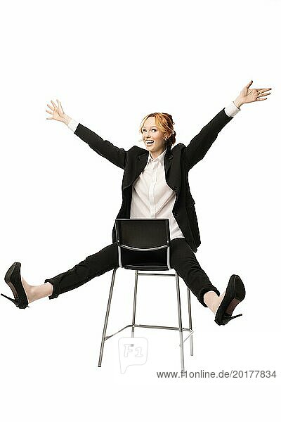 Fröhliche junge  aufgeregte Managerin mit rothaarigem Anzug  die lächelt und in die Kamera schaut  während sie mit ausgestreckten Armen auf einem Stuhl sitzt