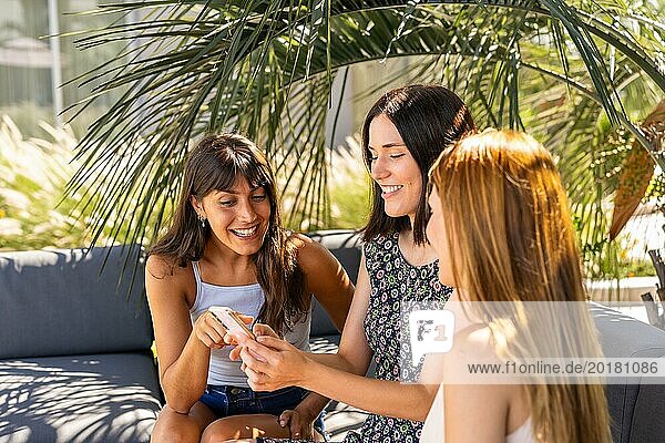 Seitenansicht von drei schönen Frauen  die auf einem Sofa sitzend etwas auf ihrem Smartphone ansehen