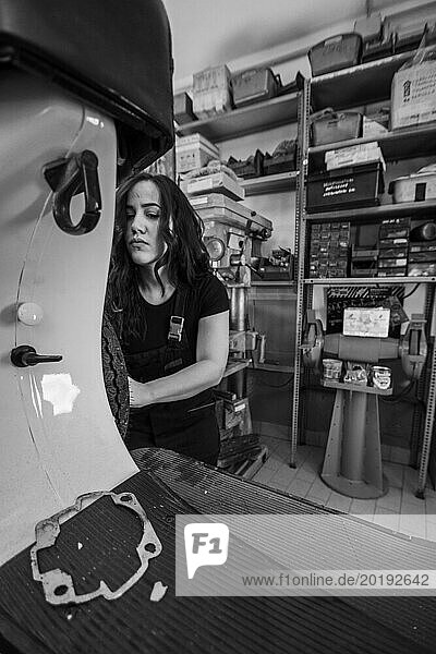 Serious woman mechanic disassembling a part on a moped italian vintage scooter motorcycle in the workshop  real women performing traditional man jobs of the past  black and white photograph