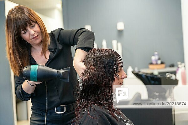 Seitenansicht einer reifen Friseurin  die das Haar einer Kundin im Salon ordnet und trocknet