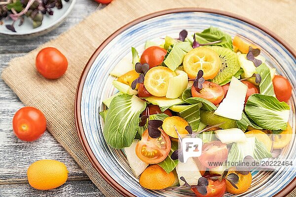 Vegetarian salad of pac choi cabbage  kiwi  tomatoes  kumquat  microgreen sprouts on gray wooden background and linen textile. Top view  close up  selective focus