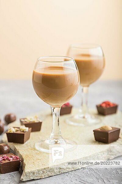 Sweet chocolate liqueur in glass with chocolate candies on a gray concrete background and stone slate board. Side view  close up  selective focus