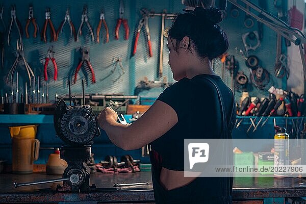 Geschickte Handwerkerin bei der Reparatur eines Motorradmotorteils in einer Werkstatt mit blaugrüner Wand  eine komplette Werkzeugtafel im Hintergrund mit Bokeh Effekt  traditionelle Männerberufe von Mixed race latino woman