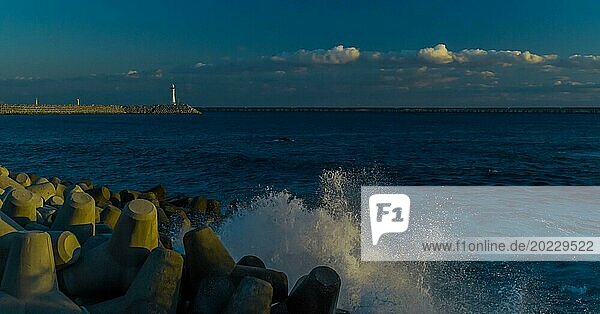 Evening view of a calm seashore with spray over tetrapods  lighthouse in the background  in South Korea
