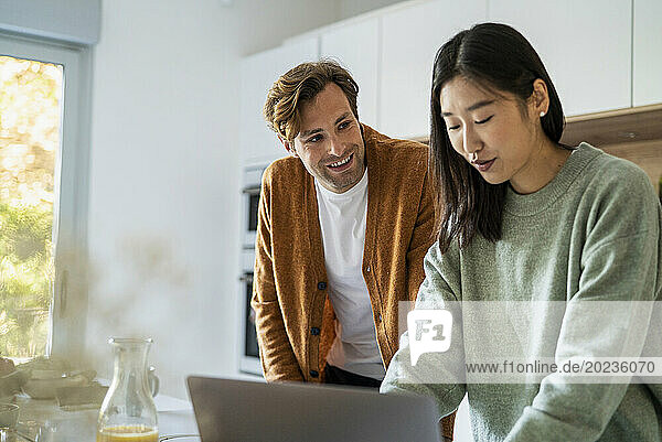 Adult couple shopping online on laptop while leaning on kitchen counter