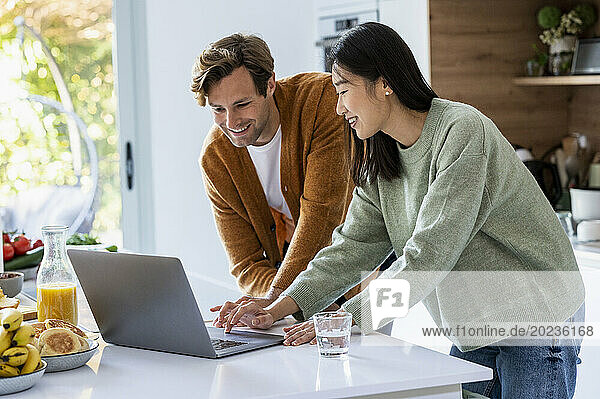 Adult couple using laptop together at kitchen counter