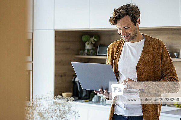 Adult man using laptop while standing in kitchen