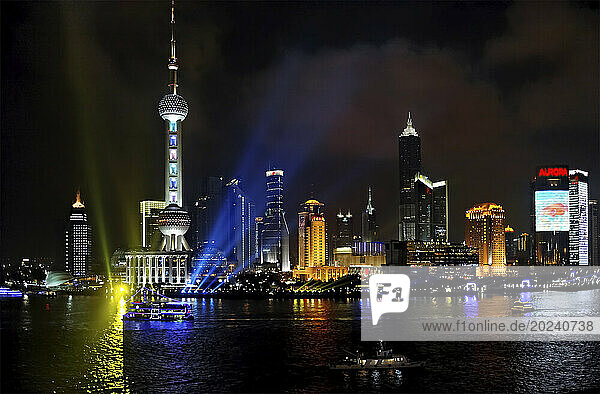 Shanghai at night where buildings are illuminated and boats glide on the water near new construction along the Dong Da Ming Road; Shanghai  People's Republic of China