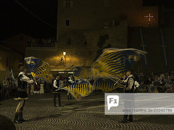 Flag-wavers dressed in medieval costumes performing in a town square at night; Grottazzolina  Fermo province  Italy