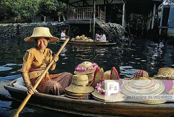 Smiling Thai woman with a canoe full of straw hats; Damnoen Saduak  Thailand