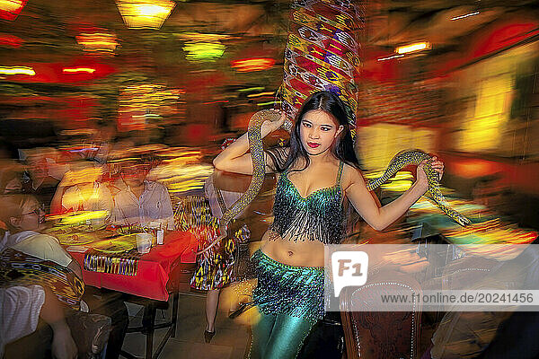 Dancer in green sparkles and fringe performs with a live snake at the Fun Ti Carnival Restaurant in Beijing. The dancers  wait staff  and performers are all migrant workers from Xinjiang Province in Northwest China. Migrant workers in China are mostly from impoverished regions who go to more urban and prosperous coastal regions in search of work. China has been experiencing the largest mass migration in history and people have left the countryside for the cities-perhaps 400 million people by 2025. Many are farmers and farm workers made obsolete by modern farming practices and factory workers who have been laid off from inefficient state-run factories; Beijing  People's Republic of China