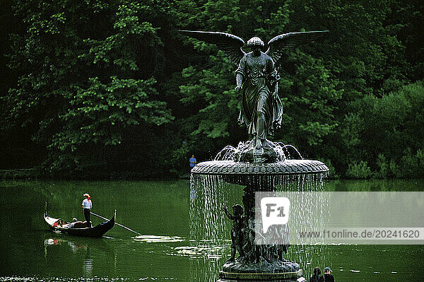 Gondola drifts in the lake beyond 'Angel of the Waters'  a fountain rising from Bethesda Terrace that was created by sculptor Emma Stebbins (1815-1882)  the first woman to receive a commission for a major public work in New York City. Bethesda Fountain  as it is commonly known  stands twenty-six feet high and ninety-six feet in diameter  and is one of the largest fountains in New York. Designers Frederick Law Olmsted and Calvert Vaux considered Bethesda Terrace to be the heart of Central Park. Stebbins worked on the design of the statue in Rome from 1861 until its completion seven years later. Cast in Munich  it was dedicated in Central Park celebrating the 1842 opening of the Croton Aqueduct  which brought fresh water from Westchester County into New York City. Stebbins likened the healing powers of the biblical pool to that of the pure Croton water that cascades from the fountain. The lily in the angel’s hand represents purity  while the four figures below represent Peace  Health  Purity  and Temperance; New York City  New York  United States of America