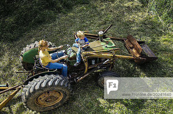 Mother drives farm equipment with young son riding along; Schuyler  Nebraska  United States of America