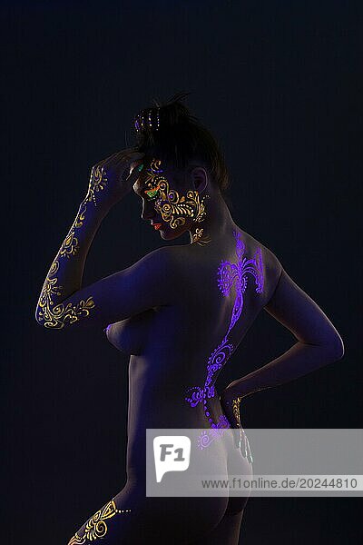 Seitenansicht eines schlanken Mädchens mit leuchtendem UV Muster auf dem Körper