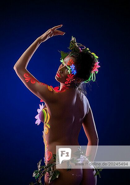Sinnliche Frau posiert mit uv leuchtenden Blumen in der Dunkelheit